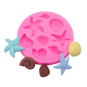 May include: Pink silicone mould with 10 different shapes of seashells and starfish. The mould is filled with colourful candy replicas of the shapes.
