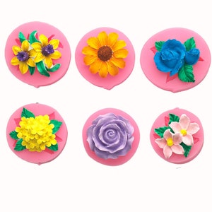 May include: Six silicone moulds for making flower-shaped cakes or decorations. The moulds are pink and feature different flower designs, including a sunflower, a rose, and a cluster of small flowers.