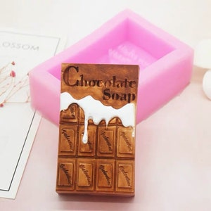 May include: A pink silicone mould for making chocolate soap. The mould is shaped like a chocolate bar with white chocolate dripping down the sides. The text "Chocolate Soap" is engraved on the top of the bar.