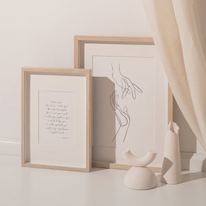 May include: Two framed prints with a minimalist design. The print on the left features a quote about strength and support. The print on the right features a line drawing of two hands reaching towards each other.