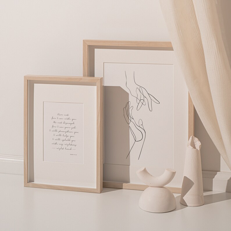May include: Two framed prints with a minimalist design. The print on the left features a quote about strength and support. The print on the right features a line drawing of two hands reaching towards each other.