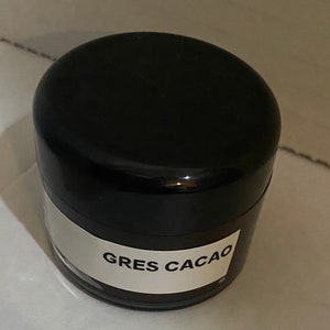 May include: A black jar with a white label that reads "GRES CACAO".