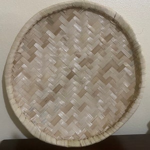 May include: A round woven tray made of natural materials with a light brown color and a woven pattern. The tray is perfect for serving food or displaying decorative items.