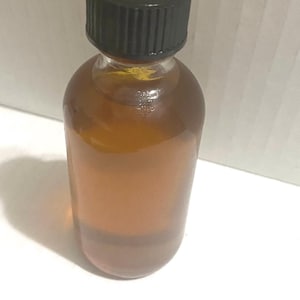 May include: A clear glass bottle with a black screw-on cap filled with a light brown liquid.