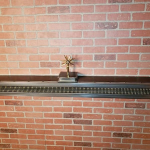 May include: A metal shelf with a black top and a decorative metal trim. The shelf is mounted on a brick wall. A gold metal star-shaped object is on top of the shelf.
