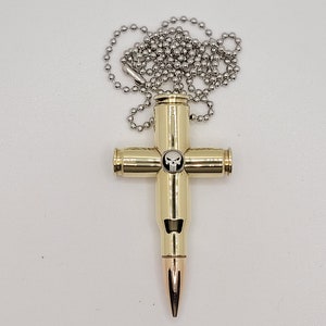 May include: A gold-colored bullet casing cross pendant with a silver skull design, hanging from a silver chain.