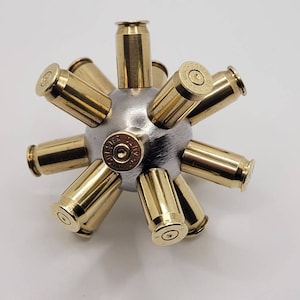 May include: A silver metal sphere with eight brass bullet casings attached to it. The casings are arranged in a starburst pattern.