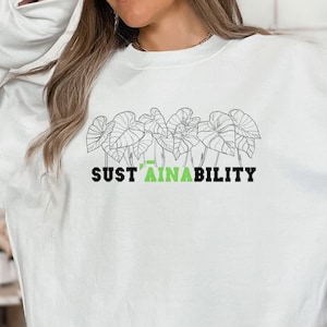 Op de afbeelding: Wit sweatshirt met een groene afbeelding van bladeren en de tekst "SUST'AINABILITY" gedrukt op de voorkant.