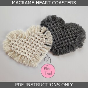 May include: Two macrame heart coasters, one in white and one in gray, with fringe around the edges. The text "Make These!" is written on a pink circle.