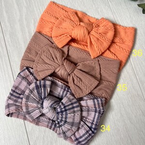 Op de afbeelding: Drie stoffen hoofdbanden met strikken. De bovenste hoofdband is perzikkleurig, de middelste hoofdband is bruin en de onderste hoofdband is geruit met roze, grijs en zwart.