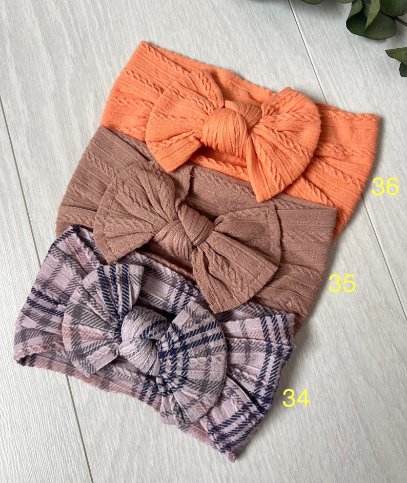 Op de afbeelding: Drie stoffen hoofdbanden met strikken. De bovenste hoofdband is perzikkleurig, de middelste hoofdband is bruin en de onderste hoofdband is geruit met roze, grijs en zwart.