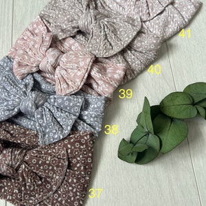 Op de afbeelding: Vier stoffen hoofdbanden met een bloemenpatroon en een strik. De hoofdbanden zijn in de kleuren bruin, grijs, roze en beige. De hoofdbanden zijn genummerd 37, 38, 39, 40 en 41.