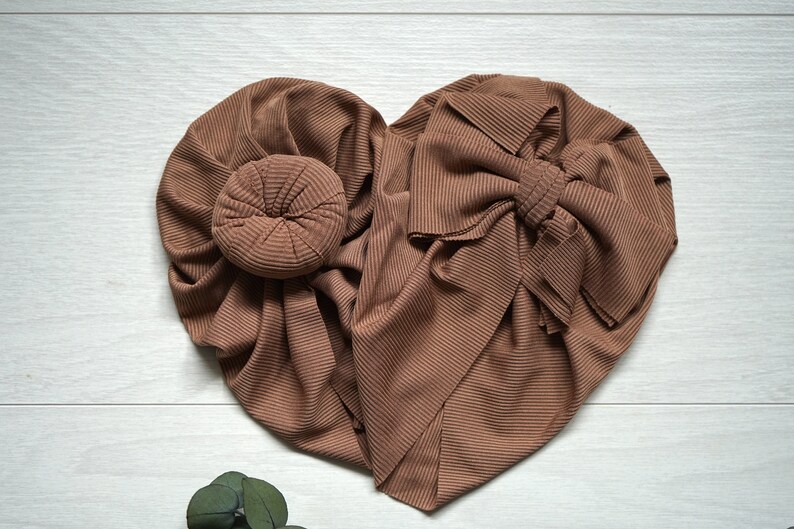 May include: Two brown ribbed fabric headbands, one tied in a bow and the other with a bun-shaped center.