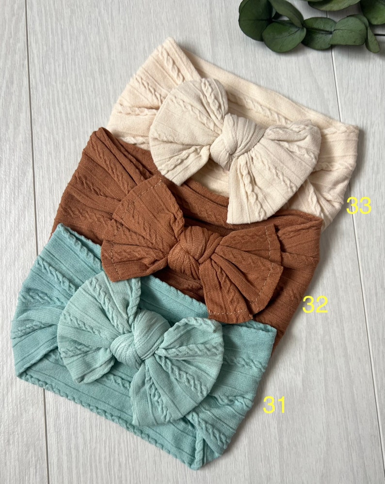 Op de afbeelding: Drie stoffen hoofdbanden met een geknoopt strikdesign. De hoofdbanden zijn in de kleuren bruin, beige en lichtblauw. De nummers 31, 32 en 33 staan op de afbeelding.
