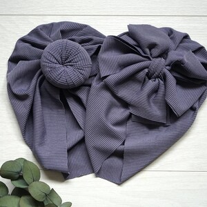 May include: Two gray fabric headbands, one with a bun and the other with a bow. The headbands are made of a ribbed fabric.