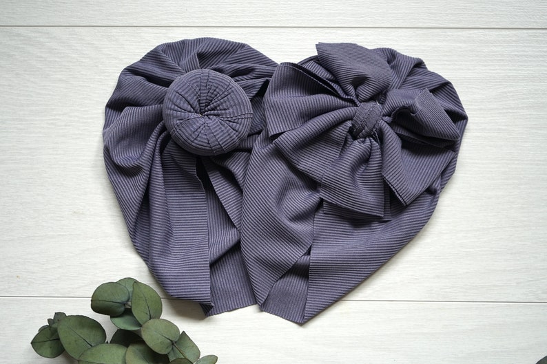 May include: Two gray fabric headbands, one with a bun and the other with a bow. The headbands are made of a ribbed fabric.