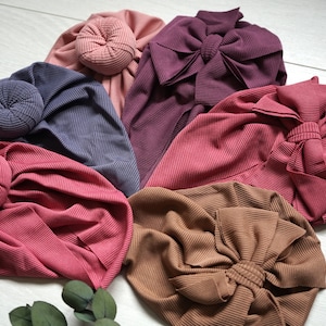 May include: Six different colors of fabric headbands with a knotted bow or bun detail. The colors are dusty rose, mauve, burgundy, brown, dark gray, and light pink.
