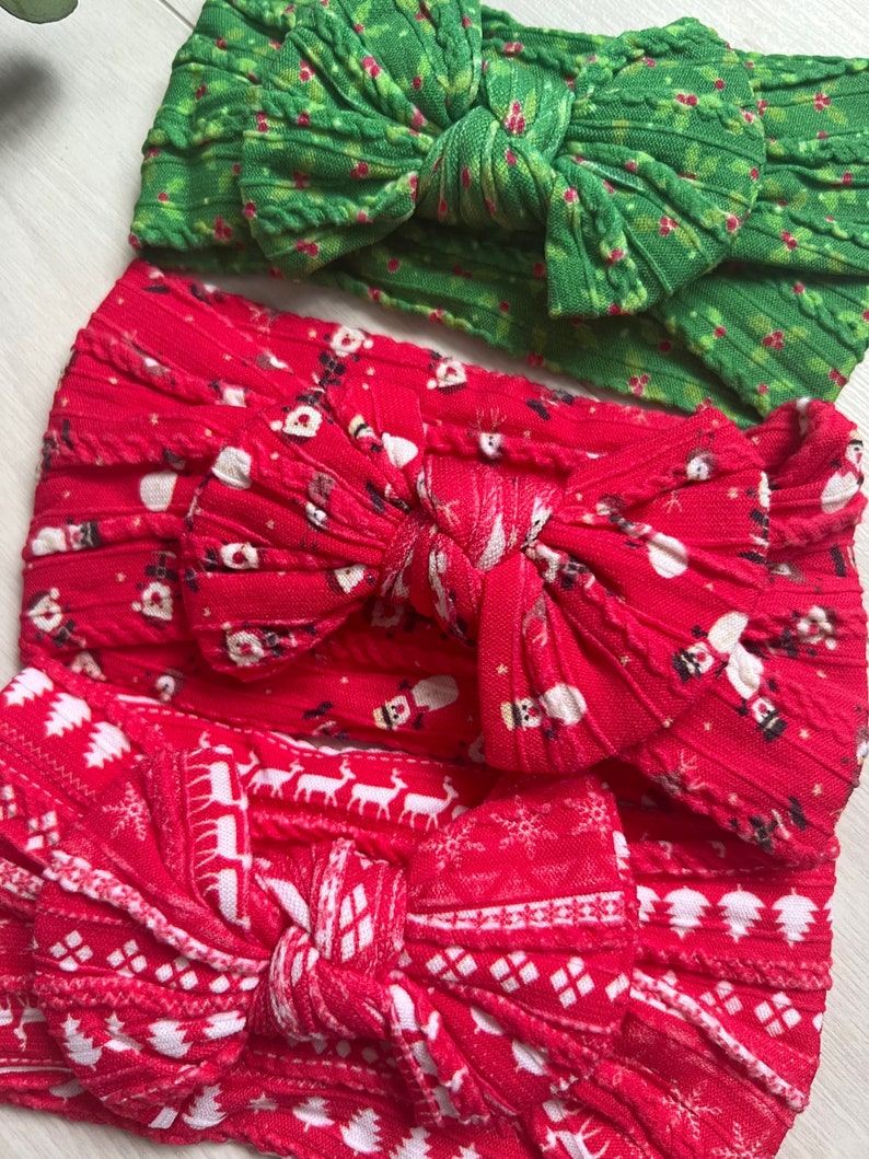 Op de afbeelding: Drie kerstthema hoofdbanden met rode en groene stof. De hoofdbanden zijn gebonden in een strik en hebben verschillende patronen, waaronder sneeuwvlokken, rendieren en hulst.