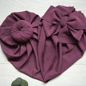 May include: Two mauve fabric headbands, one with a large bow and the other with a bun. The headbands are made of a ribbed fabric.
