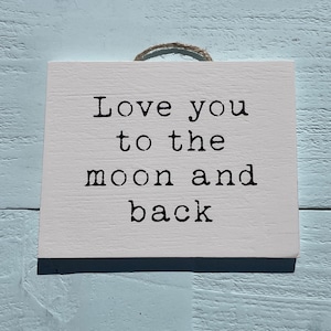 Puede incluir: Un letrero de madera blanco con texto negro que dice "Love you to the moon and back".