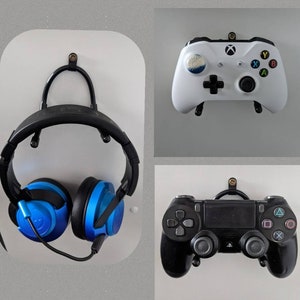 May include: A white wall with three different gaming accessories mounted on it. A black headset with blue earcups, a white Xbox controller, and a black Playstation controller.