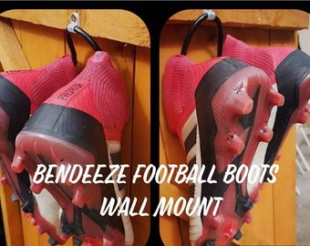 Könnte beinhalten: Zwei Paar rot-schwarze Fußballschuhe, die an einer Wandhalterung hängen. Die Schuhe sind mit "Predator" beschriftet. Der Text "Bendeezee Football Boots Wall Mount" steht unter den Schuhen.