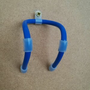 K&ouml;nnte beinhalten: Ein blauer, U-f&ouml;rmiger Wandhalter mit transparenten Kunststoffclips und Endkappen. Der Halter ist mit einer Schraube an einer hellbraunen Oberfl&auml;che befestigt.