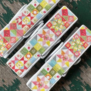 May include: Four white wooden clothespins with a colorful patchwork design. The design features a variety of colors, including red, pink, yellow, green, and blue. The clothespins are perfect for adding a touch of whimsy to your home decor.