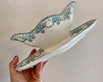 May include: A white ceramic gravy boat with a green floral design. The boat has a matching saucer.