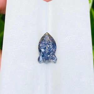 May include: A blue and silver gemstone with a teardrop shape and a pointed tip. The gemstone is set in a clear, faceted setting.