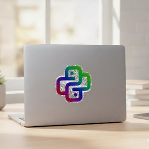 Op de afbeelding: Een zilveren laptop met een Python-sticker. De sticker is een kleurrijk, glinsterend Python-logo in groen, blauw, paars en rood. De laptop staat op een houten oppervlak met een plant en boeken op de achtergrond.