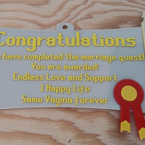 May include: A light grey scroll-shaped wall plaque with yellow pixelated text that reads: Congratulations, You have completed the marriage quest! You are awarded: Endless Love and Support, 1 Happy Life, Same Vagina forever. A red and yellow ribbon seal.