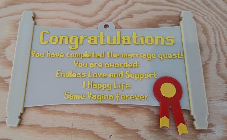 May include: A light grey scroll-shaped wall plaque with yellow pixelated text that reads: Congratulations, You have completed the marriage quest! You are awarded: Endless Love and Support, 1 Happy Life, Same Vagina forever. A red and yellow ribbon seal.