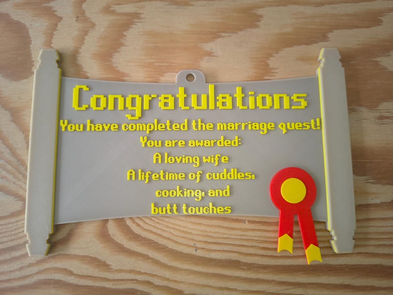 May include: A light grey scroll-shaped plaque with yellow pixelated text that reads: Congratulations, You have completed the marriage quest! You are awarded: A loving wife, A lifetime of cuddles, cooking, and butt touches. A red and yellow ribbon is attached.