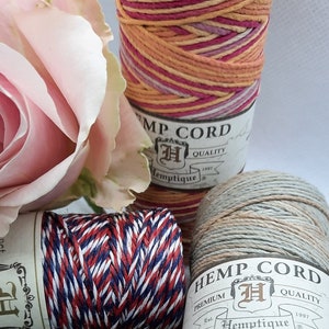 May include: Three spools of hemp cord, each with a different color pattern. The spools are labeled "Hemp Cord" with the company logo and "Premium Quality" in a vintage style font. The colors of the cords are pink, orange, and white; red, white, and blue; and green, white, and beige.