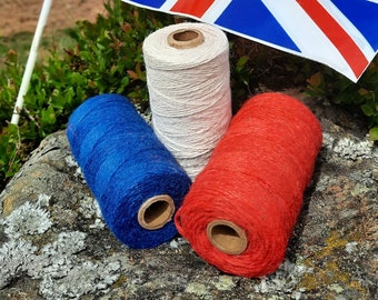 May include: Three spools of yarn in red, white, and blue, sitting on a rock with a Union Jack flag in the background.