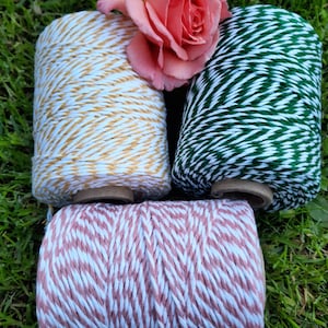 May include: Four spools of twine with different coloured stripes. The spools are arranged in a circle with a pink rose in the centre. The twine colours are yellow and white, green and white, pink and white, and brown and white.