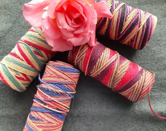 Peut inclure: Quatre bobines de fil à broder coloré, chacune avec un motif de rayures différent. Le fil est enroulé autour de bobines en carton. Une rose rose est en arrière-plan.