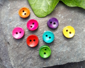 May include: Assortment of eight colorful wooden buttons in various shades of red, orange, yellow, green, blue, purple, and pink. The buttons are arranged in a semi-circle on a gray stone surface.