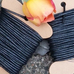 May include: Two spools of black waxed cord, each wound on a cardboard spool with a cut-out shape. The spools are sitting on a grey surface.