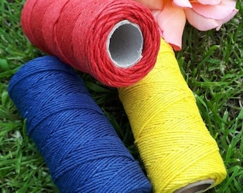 Peut inclure: Trois bobines de ficelle rouge, bleue et jaune. Les bobines sont sur un lit d'herbe verte.