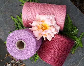 May include: Three spools of twine in different shades of pink, purple, and red. The spools are arranged on a gray surface with a pink flower in the center.