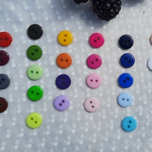 May include: Assortment of colourful two-hole buttons in various colours, including red, green, blue, yellow, purple, and white.