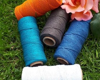 Peut inclure: Cinq bobines de ficelle de différentes couleurs : orange, bleu sarcelle, bleu foncé, gris et blanc. Les bobines sont disposées en cercle sur un lit d’herbe verte.