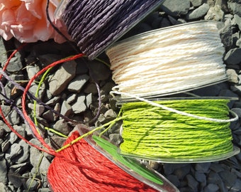 Peut inclure: Quatre bobines de ficelle de différentes couleurs : rouge, verte, blanche et violette. La ficelle est enroulée autour de bobines en plastique transparent.