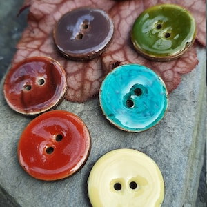 May include: Six colourful ceramic buttons with two holes each. The buttons are round and have a glossy finish. The colours are brown, purple, green, turquoise, red and yellow.