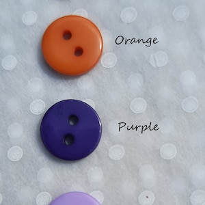May include: Four round buttons in different colors: pale yellow, orange, purple, and lilac. Each button has two holes.