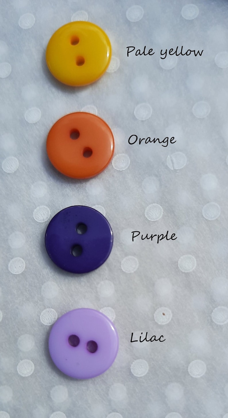 May include: Four round buttons in different colors: pale yellow, orange, purple, and lilac. Each button has two holes.