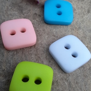 May include: Four square buttons with two holes each. The buttons are in different colours: light pink, light blue, light green, and light purple.