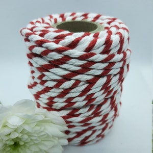 May include: A spool of red and white striped twine. The twine is tightly wound around a cardboard core. The colors are a vibrant red and clean white, creating a classic, festive look. The twine is suitable for crafts and gift wrapping.